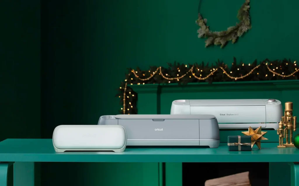 a cricut joy, cricut explore, and cricut maker on a craft table