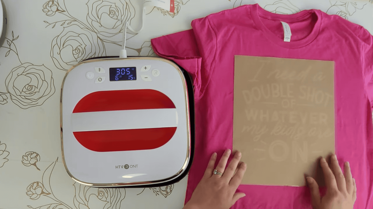 HTVRont auto heat press beside a pink t-shirt with butcher paper covering the vinyl design
