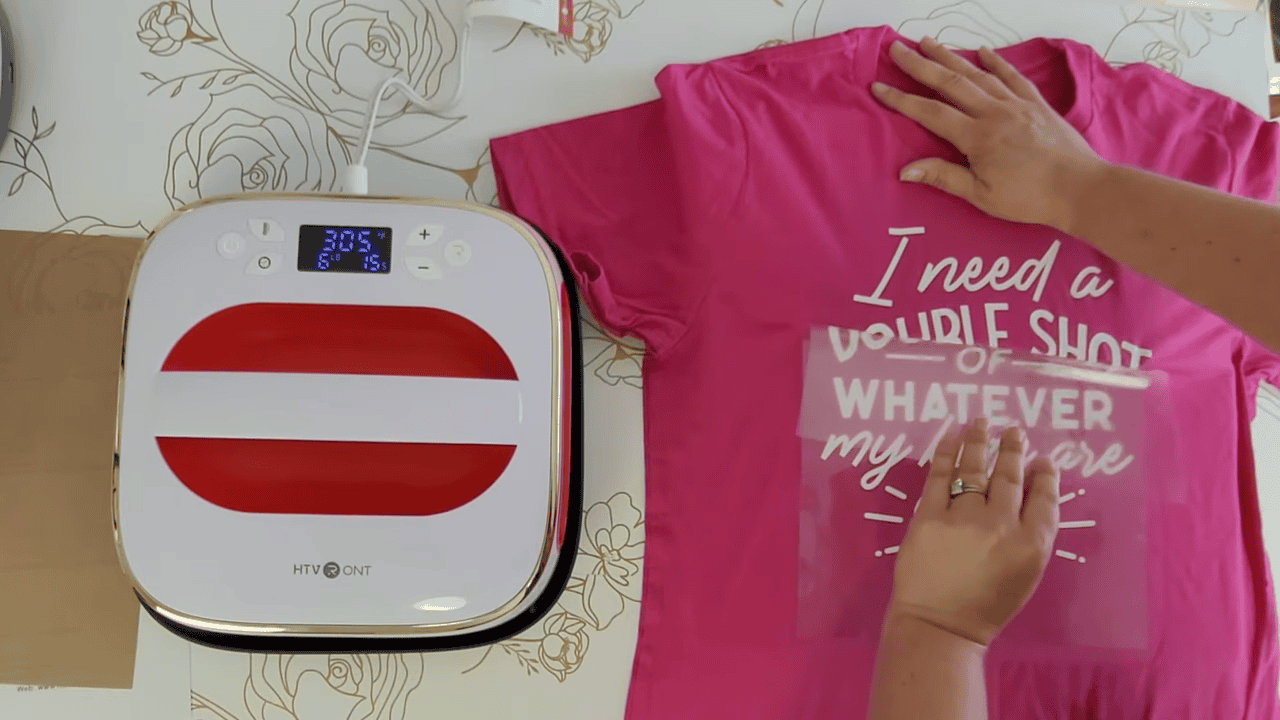Peeling the clear carrier sheet off white iron-on lettering on a pink t-shirt