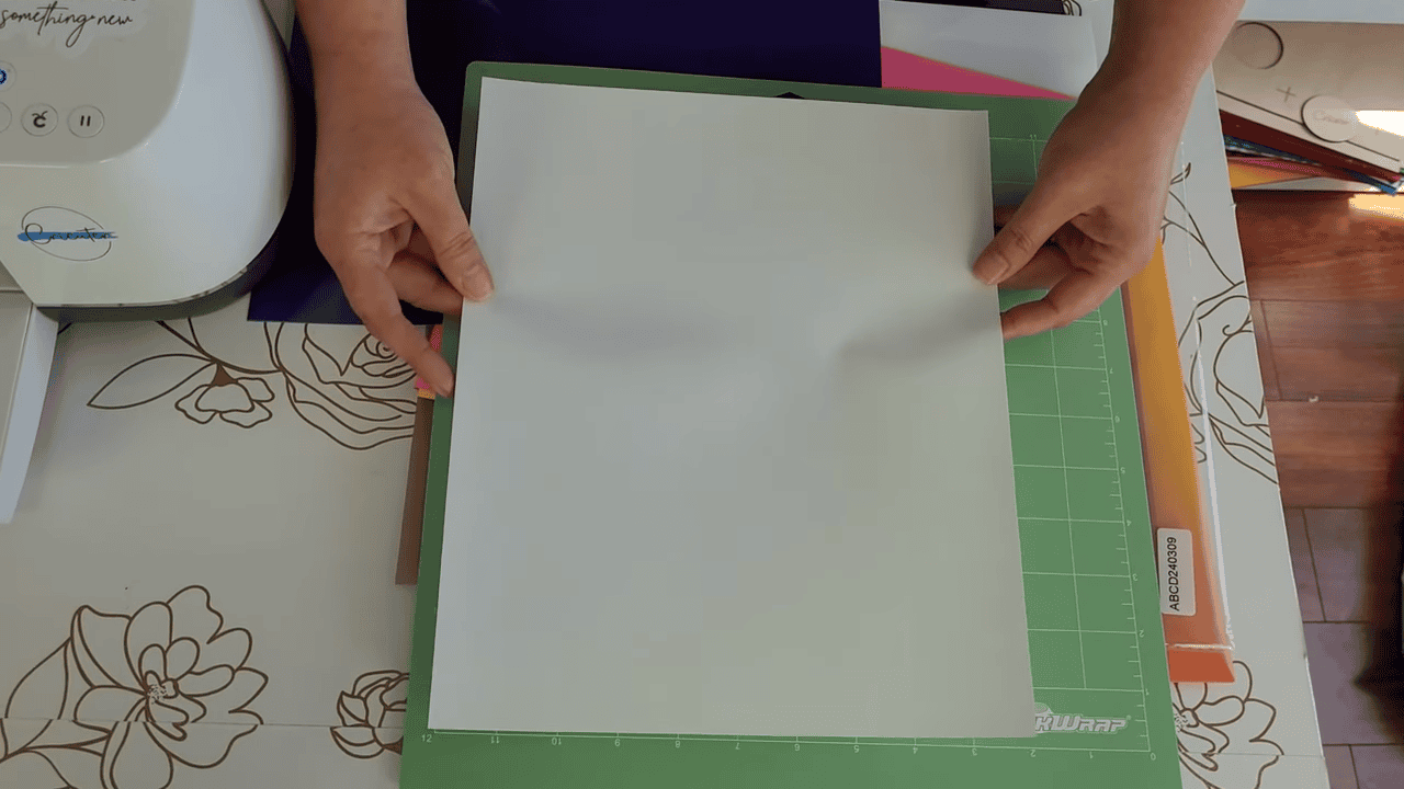 Hands placing a sheet of white heat transfer vinyl onto a green Cricut cutting mat