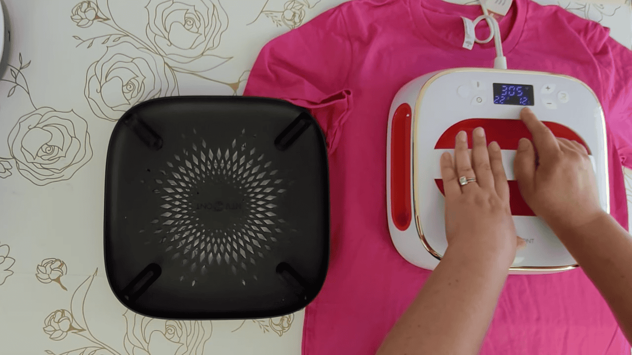 Pressing the iron-on design onto a pink t-shirt with the HTVRont auto heat press set to 305 degrees