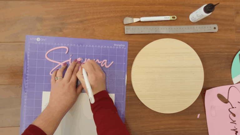 Weeding a pink craft foam name cutout on an HTVRont StrongGrip cutting mat.