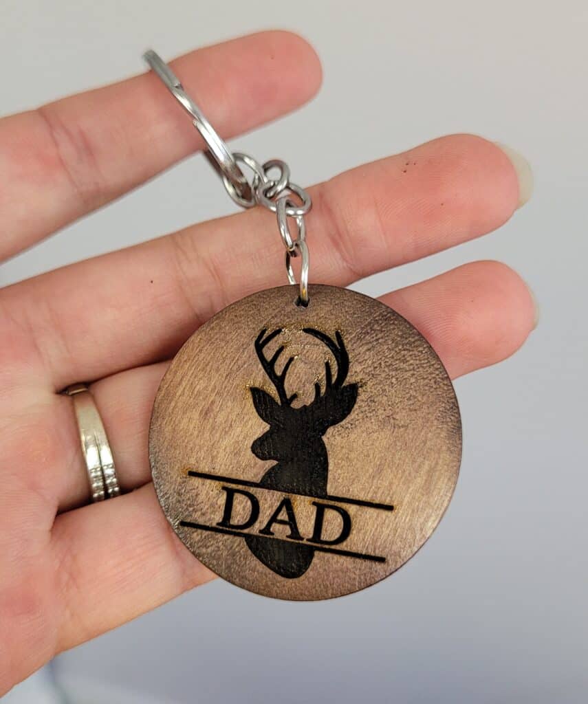 Hand holding a wooden keychain laser engraved with a deer silhouette and the word DAD, made with the WeCreat Vista laser cutter