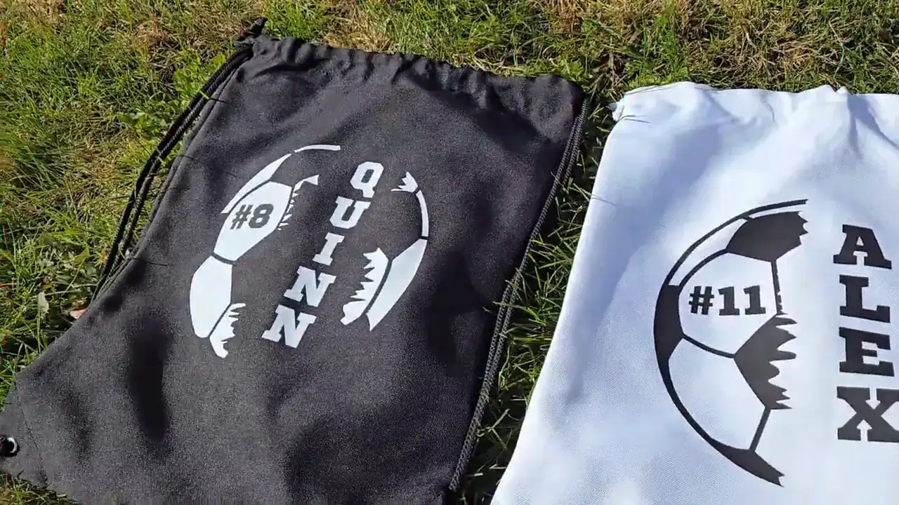 Two personalized drawstring sports bags with custom soccer ball monogram designs printed using xTool Apparel Printer, showing player names and numbers on grass.