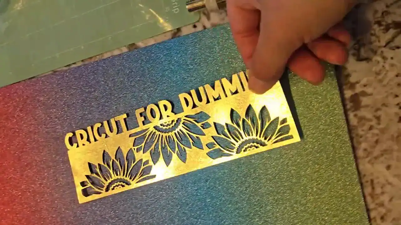 Hand holding gold foil bookmark cutout labeled Cricut For Dummies above pink-gold gradient glitter cardstock backing showing two-layer assembly