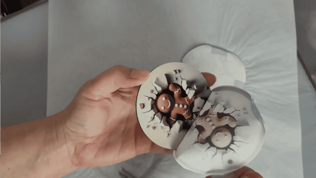 Holding finished sublimation ornaments showing the funny 3D gingerbread man design - front shows smiling face breaking through, back shows the gingerbread booty with matching cracked surface effect