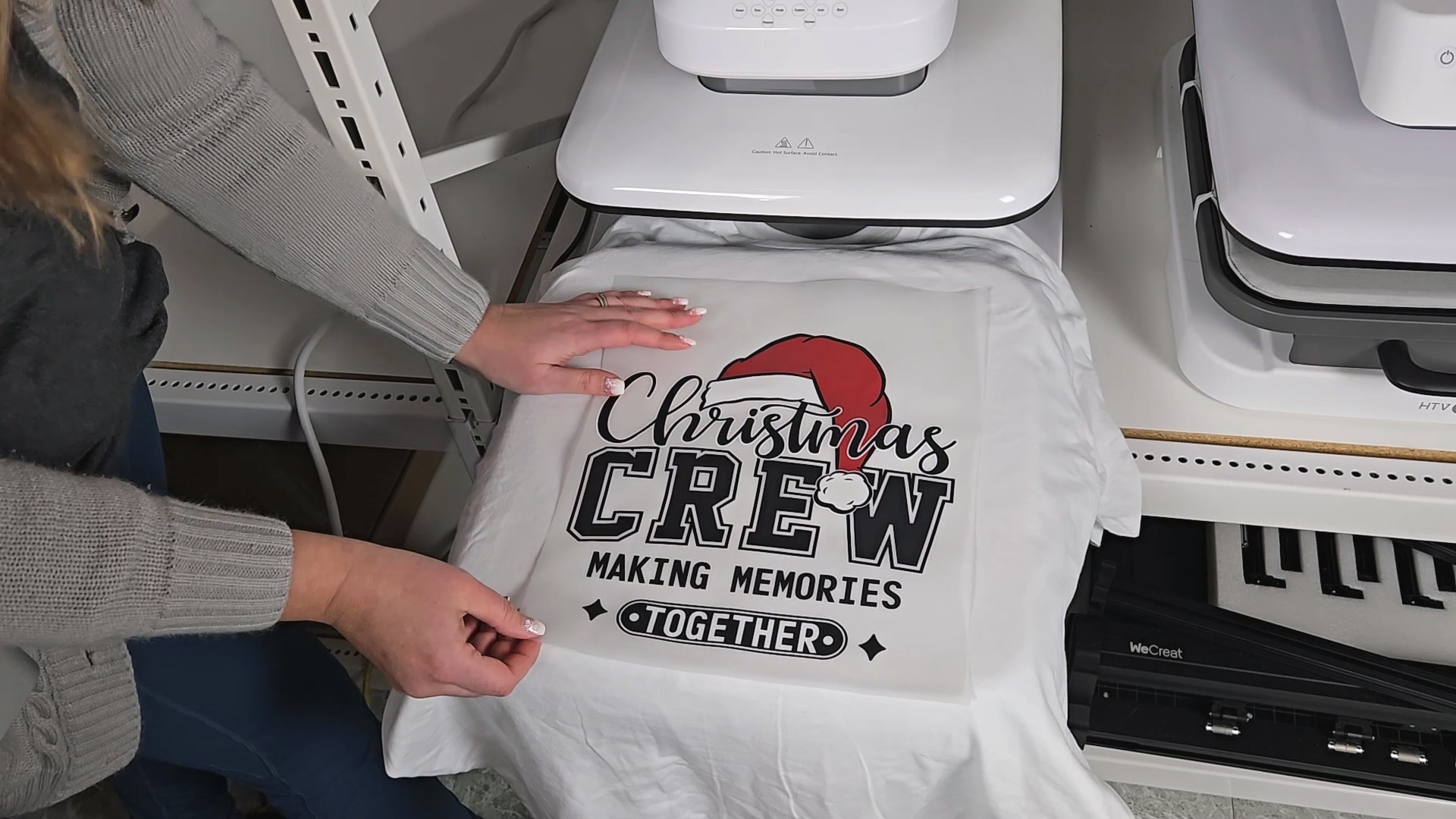 Finished white t-shirt with Christmas Crew Making Memories Together design featuring Santa hat, displayed on heat press in craft room