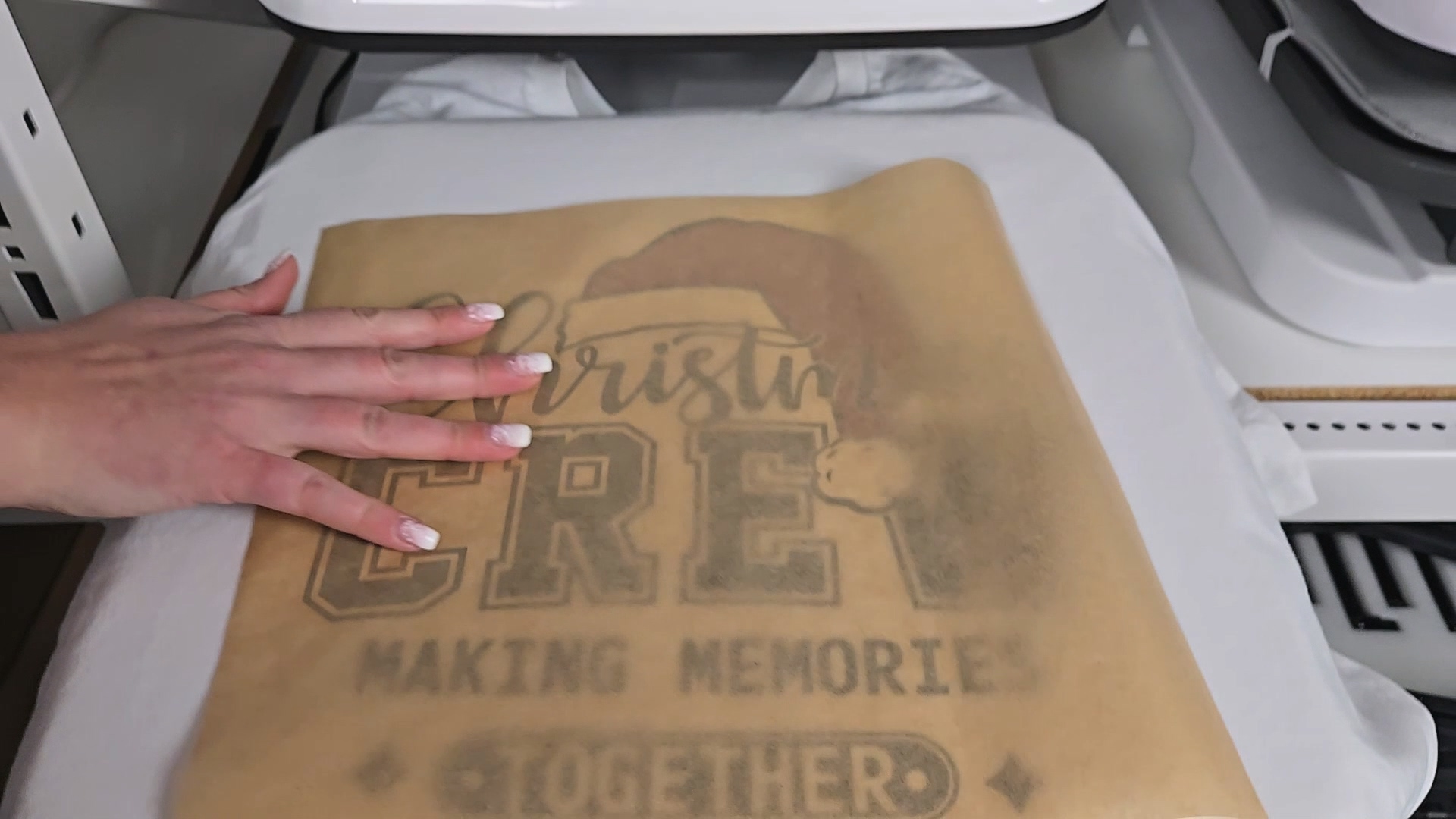 Kerri Adamczyk's Hand smoothing butcher paper over Christmas Crew DTF transfer on white t-shirt before heat pressing, showing proper pressing technique