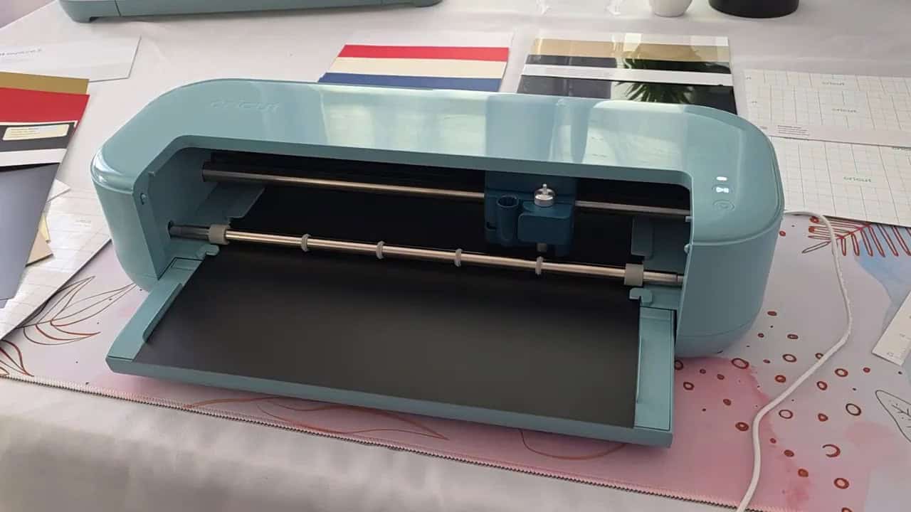 Clear front view of a teal Cricut Explore 5 with smart vinyl inserted, showing the open top and rollers.