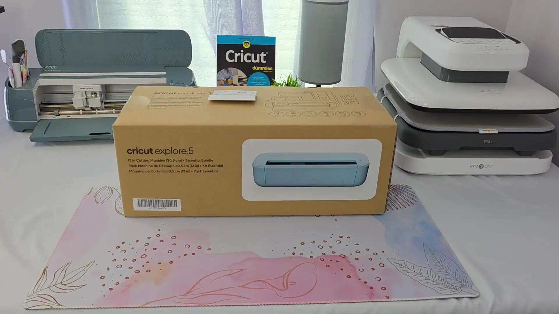 Cricut Explore 5 Essential Bundle box on a craft desk next to a Cricut Maker 4 and a copy of Cricut For Dummies
