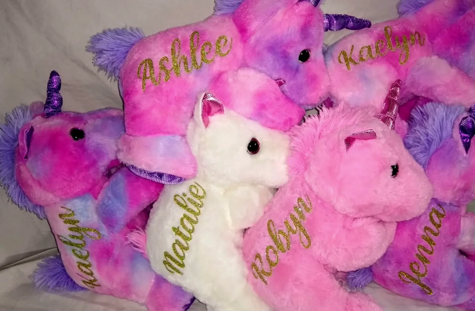 Six personalized unicorn stuffed animals with kids names cut in gold glitter vinyl with a Cricut