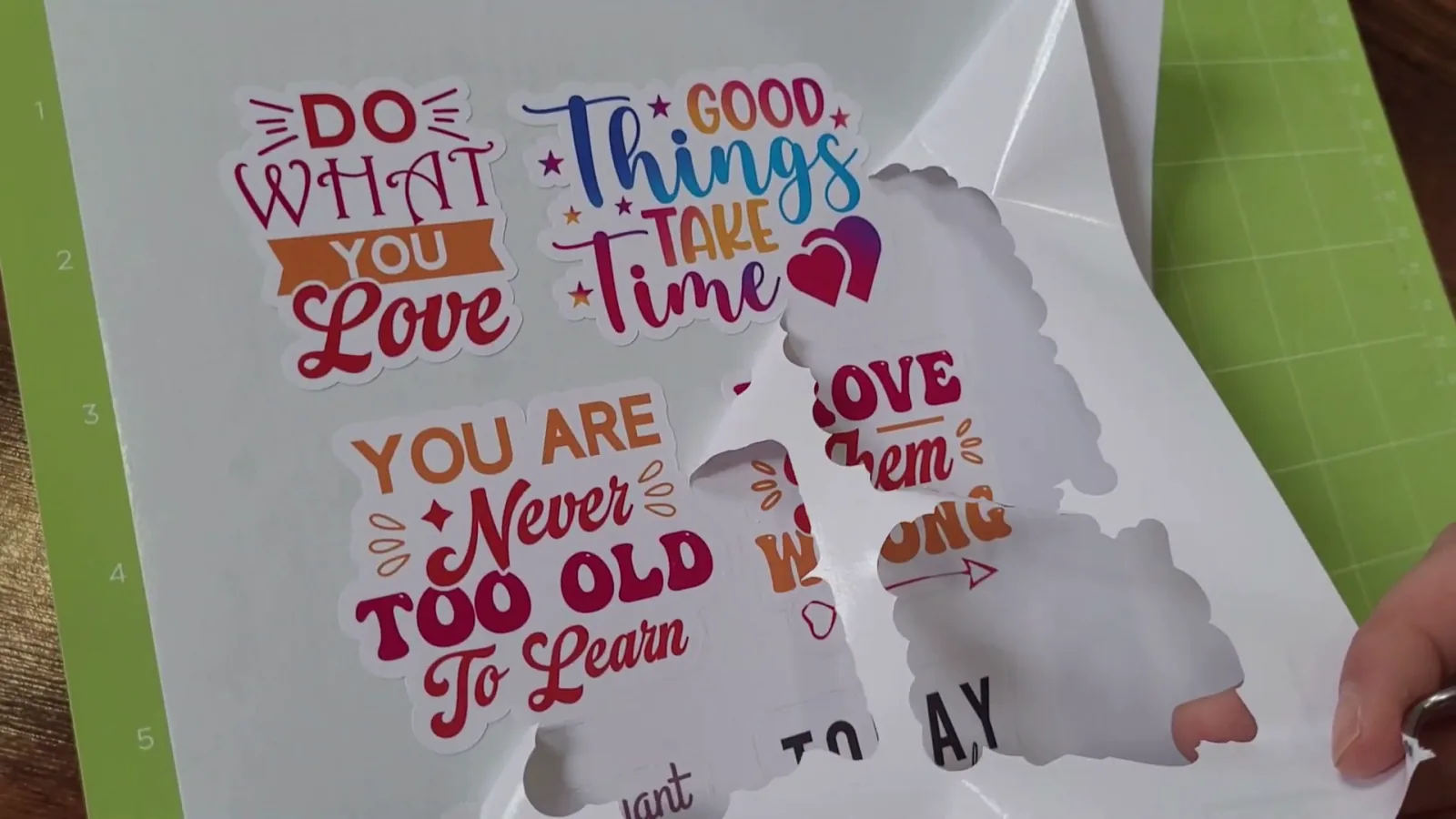 Peeling the excess printable vinyl away from a sheet of cut stickers on a Cricut mat