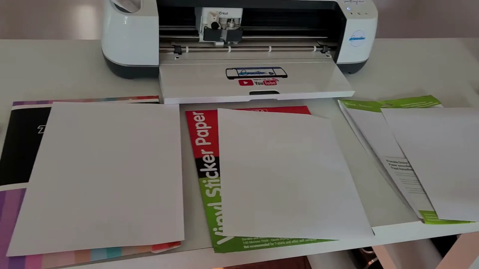 Five brands of printable sticker paper and printable vinyl laid out in front of a Cricut machine