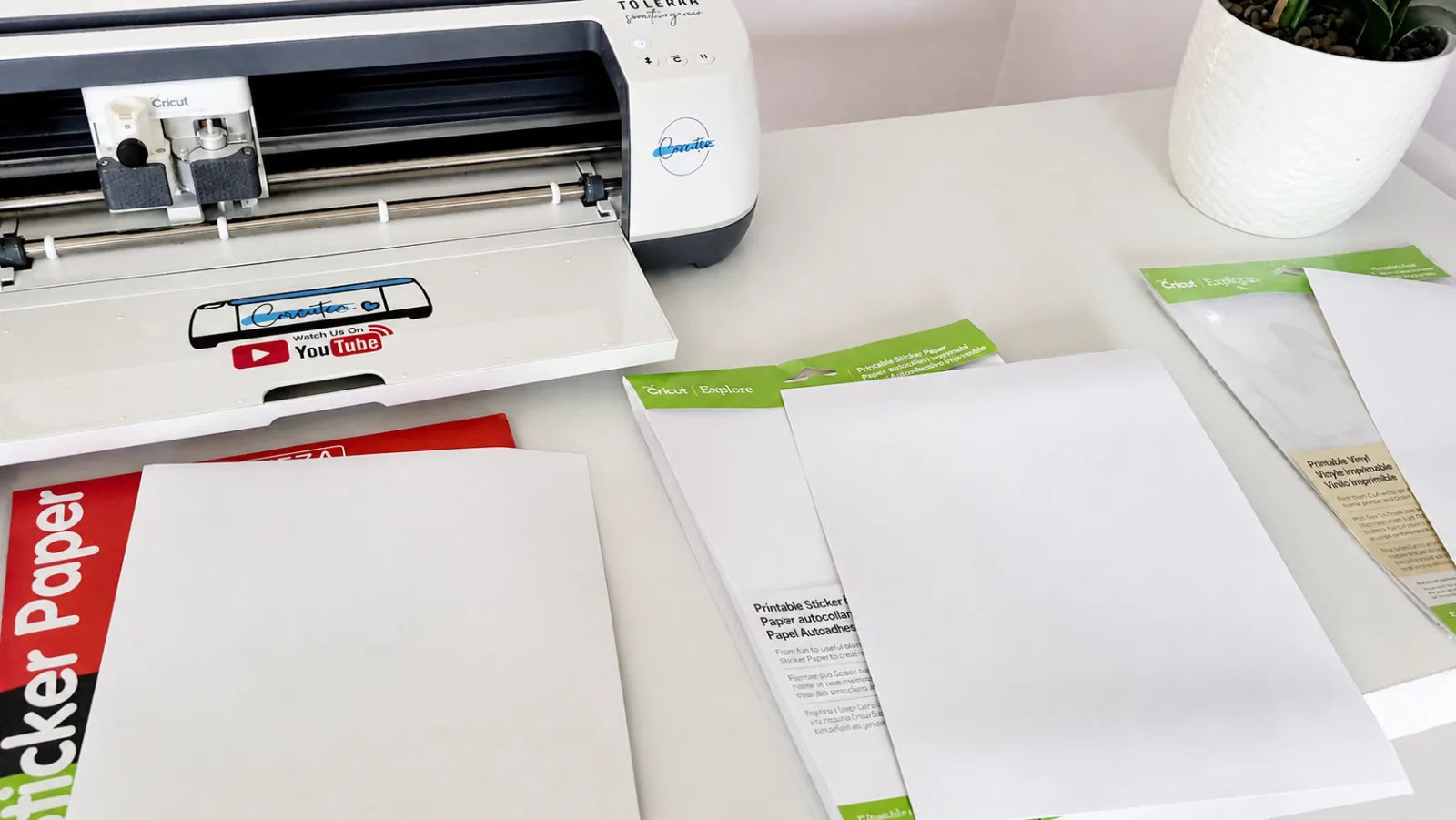 Joyeza, Cricut Printable Sticker Paper and Cricut Printable Vinyl packages laid out beside a Cricut cutting machine before testing