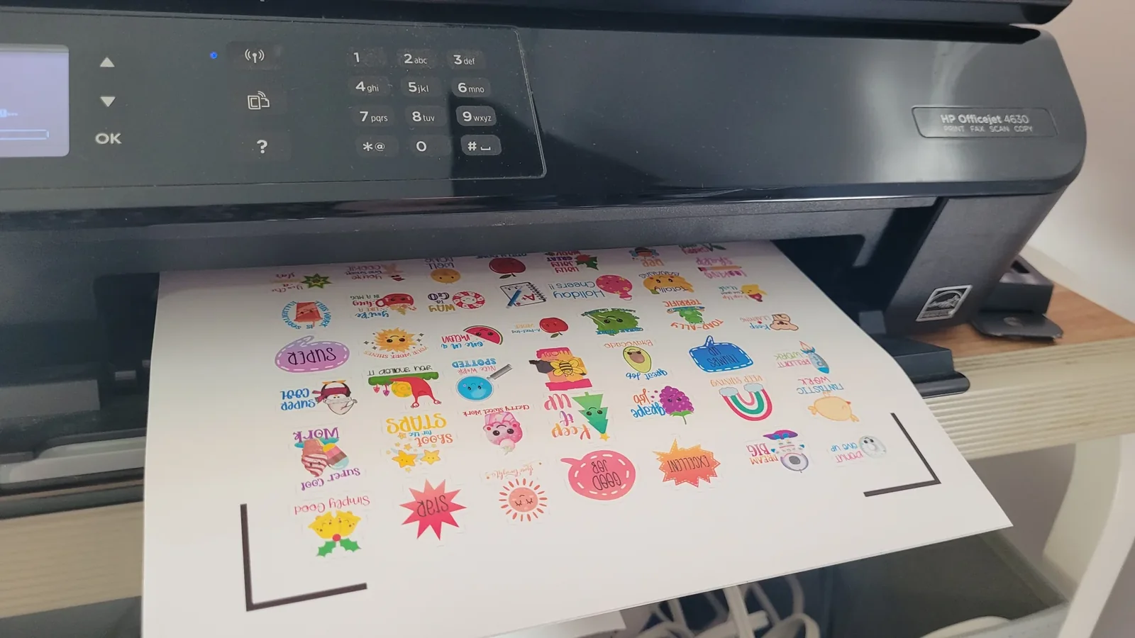 Sheet of printable sticker paper feeding out of an inkjet printer with a full page of colorful printed stickers