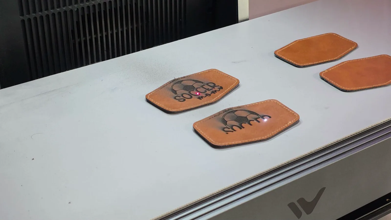 Soccer Mom leather patches spaced along the WeCreat AutoFlow conveyor for batch engraving with the MOPA laser