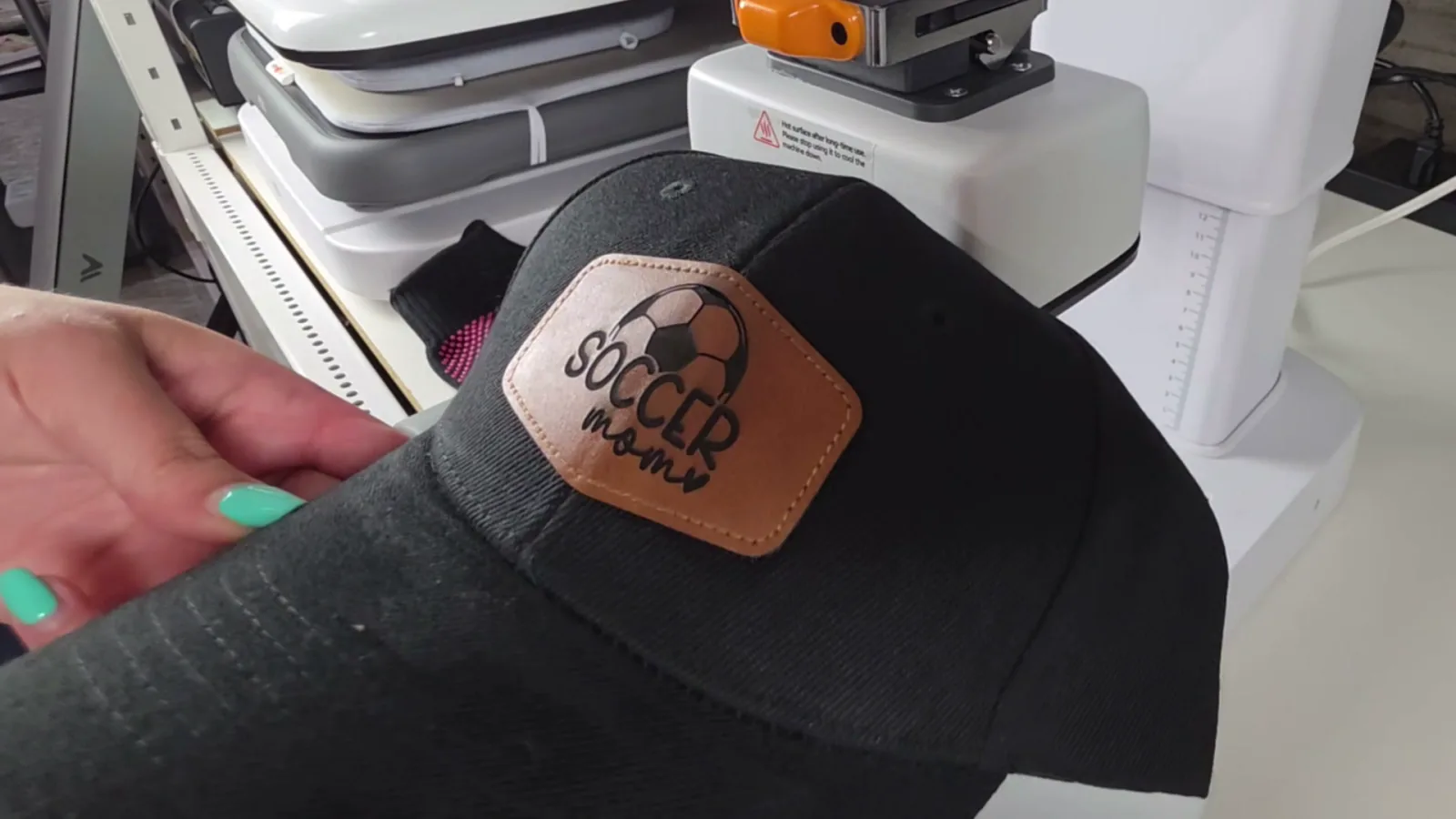 Finished Soccer Mom leather patch pressed onto a black baseball cap after engraving with the MOPA laser